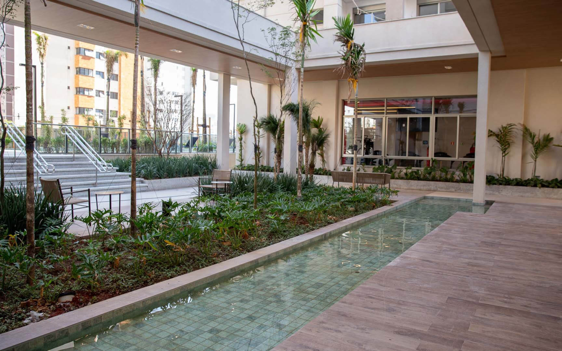 Praça central com espelho d’água, plantio exuberante e cobertura verde